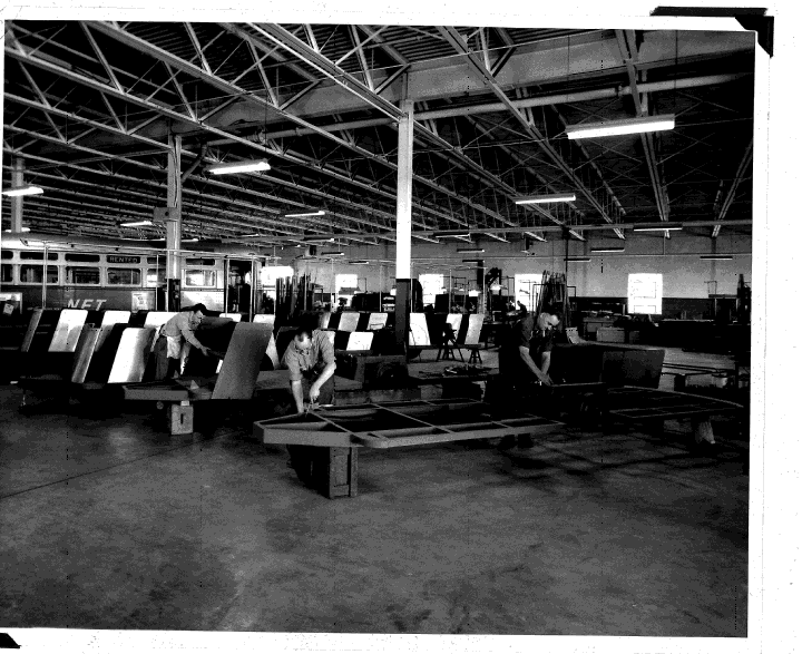 interior of a manufacturing plant showing 3 men assembling two of the viewmobile trailers, in the back ground is an old style streetcar