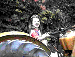 little girl sits on tractor holding steering wheel and smiling broadly